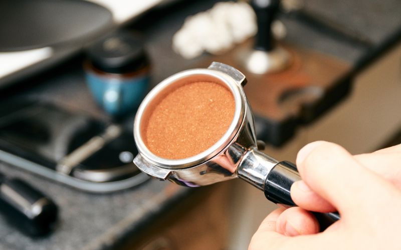 Người cầm tay cầm pha cà phê với bột cà phê đã được nén chặt, chuẩn bị pha chế trên nền bếp.