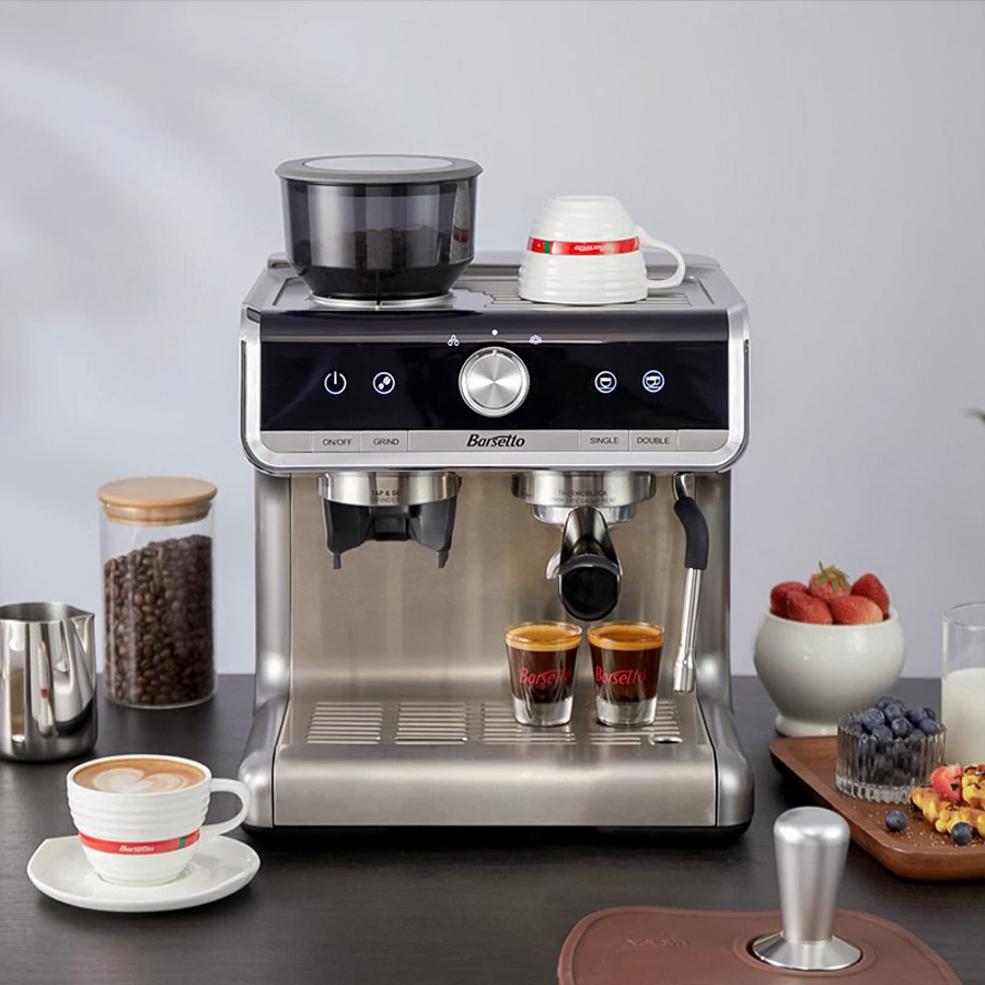 M&aacute;y pha c&agrave; ph&ecirc; tr&ecirc;n b&agrave;n với t&aacute;ch c&agrave; ph&ecirc;, hũ đựng hạt v&agrave; đĩa tr&aacute;i c&acirc;y xung quanh.