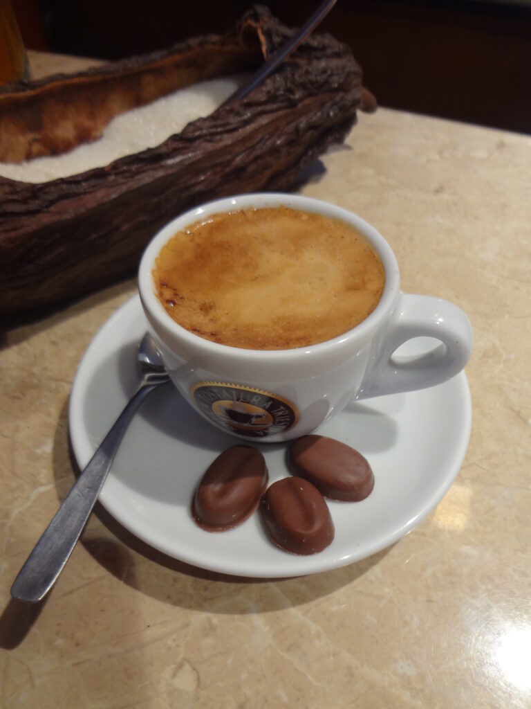 T&aacute;ch c&agrave; ph&ecirc; tr&ecirc;n dĩa trắng k&egrave;m ba vi&ecirc;n kẹo socola, nền b&agrave;n đ&aacute; cẩm thạch.