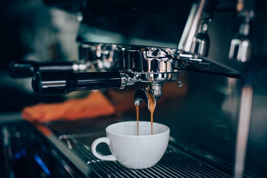 M&aacute;y pha c&agrave; ph&ecirc; đang pha chế espresso v&agrave;o một t&aacute;ch sứ trắng, với chi tiết kim loại b&oacute;ng lo&aacute;ng.