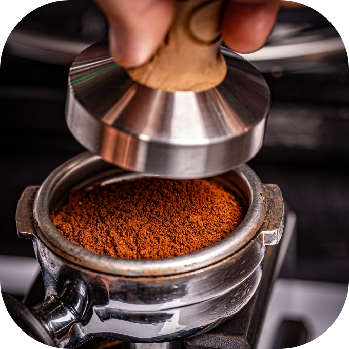 Bàn tay đang dùng dụng cụ nén cà phê trong portafilter, chuẩn bị cho máy pha cà phê espresso.