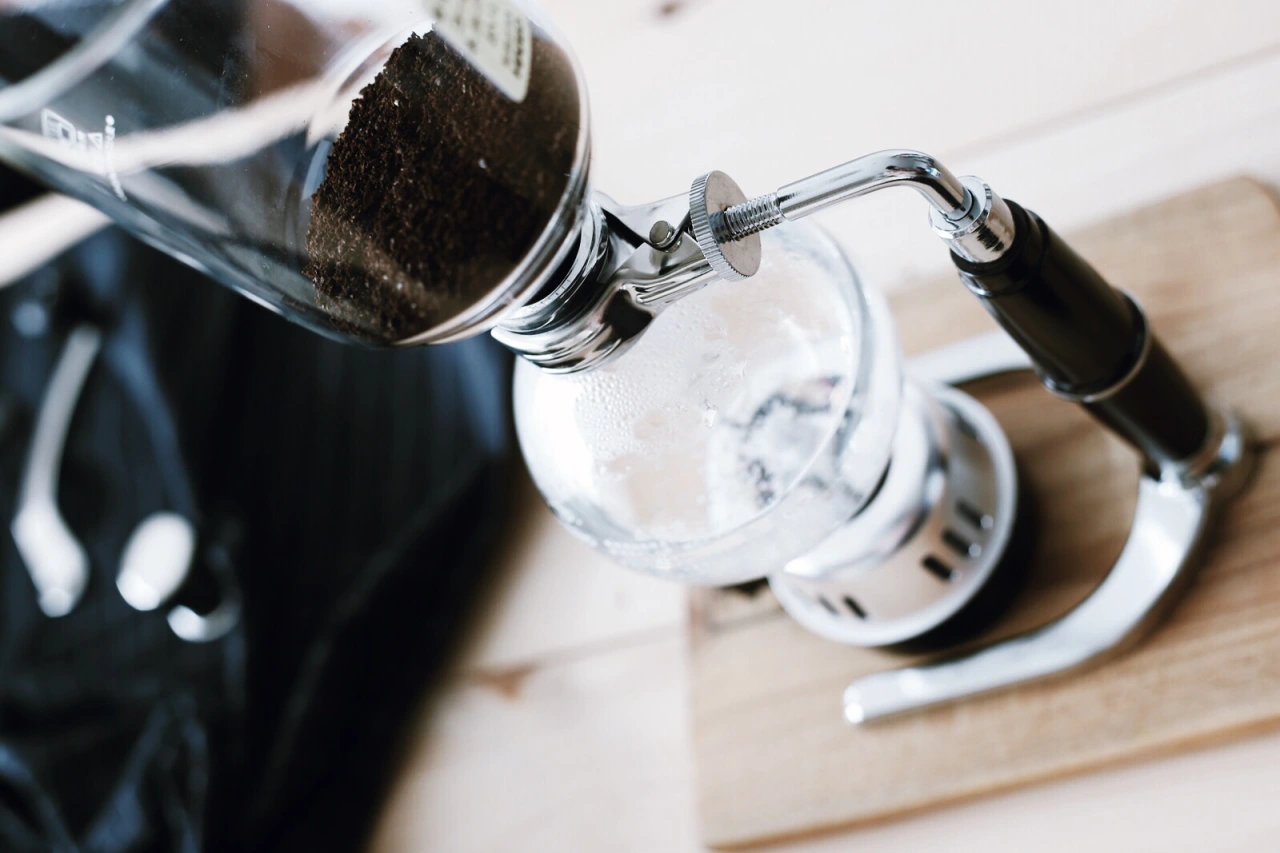 M&aacute;y pha c&agrave; ph&ecirc; syphon với c&agrave; ph&ecirc; xay b&ecirc;n trong, đặt tr&ecirc;n b&agrave;n gỗ.