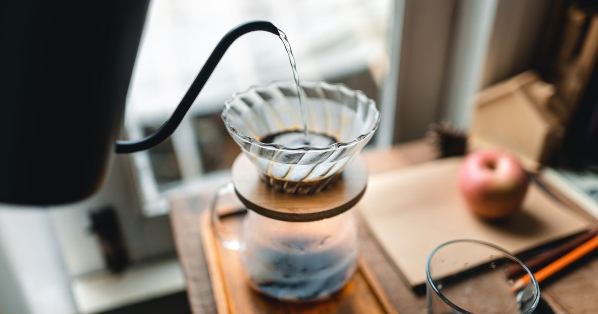 Nước đang được rót vào phễu lọc cà phê trên bàn gỗ, cạnh đó có một quả táo.