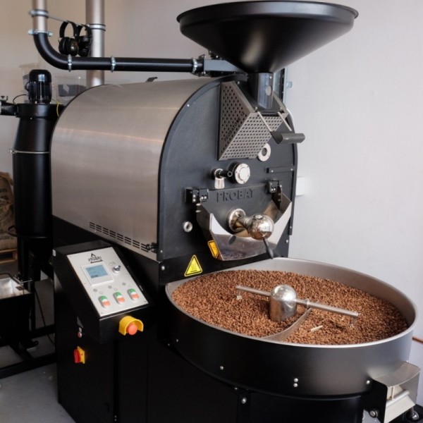 Máy rang cà phê công nghiệp với hạt cà phê đang được rang trong khay tròn phía trước.