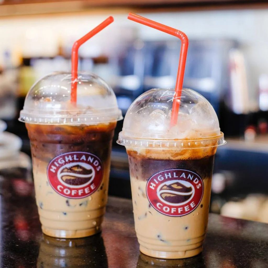 Hai ly c&agrave; ph&ecirc; sữa đ&aacute; với ống h&uacute;t đỏ, đặt tr&ecirc;n quầy, logo thương hiệu ở ph&iacute;a trước.