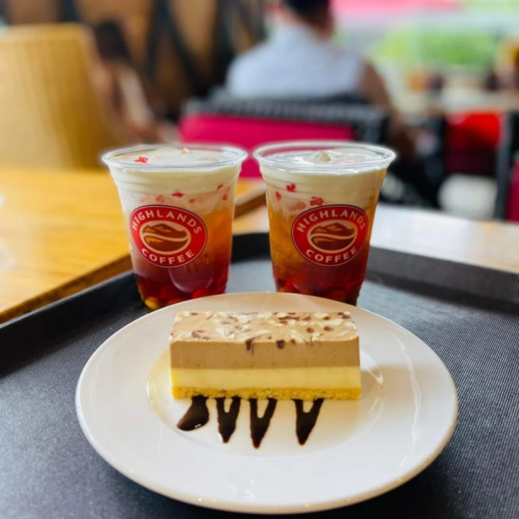 Hai ly tr&agrave; sữa v&agrave; một miếng b&aacute;nh tr&ecirc;n đĩa trắng, đặt tr&ecirc;n khay trong qu&aacute;n c&agrave; ph&ecirc;.