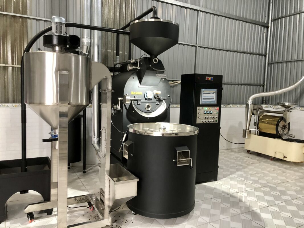 Máy rang cà phê công nghiệp trong nhà xưởng, với các thiết bị kim loại và bảng điều khiển điện tử.