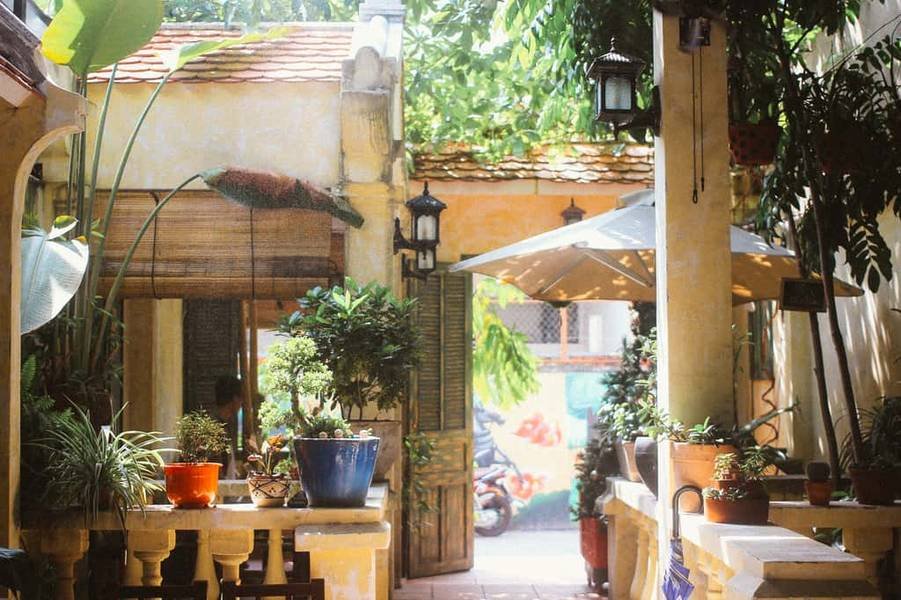 S&acirc;n vườn y&ecirc;n tĩnh với c&acirc;y xanh, chậu hoa, v&agrave; &ocirc; d&ugrave; che nắng. Đ&egrave;n trang tr&iacute; treo tr&ecirc;n cột, tạo kh&ocirc;ng gian tho&aacute;ng đ&atilde;ng.