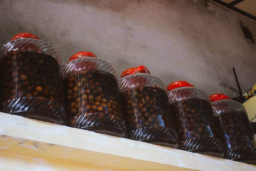 Hũ thủy tinh lớn chứa tr&aacute;i c&acirc;y ng&acirc;m, xếp h&agrave;ng tr&ecirc;n kệ, nắp đỏ.