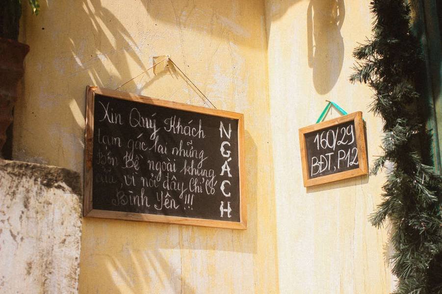 Hai bảng viết phấn treo tr&ecirc;n tường v&agrave;ng, bảng lớn c&oacute; nội dung lời nhắn, bảng nhỏ ghi địa chỉ số v&agrave; chữ.