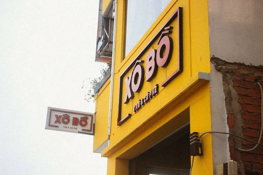 Biển hiệu qu&aacute;n tr&agrave; v&agrave; c&agrave; ph&ecirc; tr&ecirc;n nền tường m&agrave;u v&agrave;ng, g&oacute;c t&ograve;a nh&agrave; với bảng t&ecirc;n nổi bật.