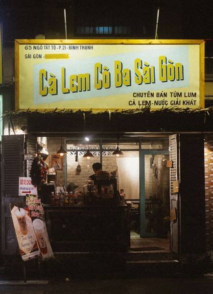 Qu&aacute;n c&agrave; lem nhỏ tại S&agrave;i G&ograve;n với biển hiệu s&aacute;ng đ&egrave;n, b&ecirc;n trong c&oacute; người đang chuẩn bị đồ uống.