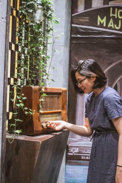 Người phụ nữ điều chỉnh radio cổ điển, b&ecirc;n cạnh l&agrave; tường trang tr&iacute; c&acirc;y xanh.