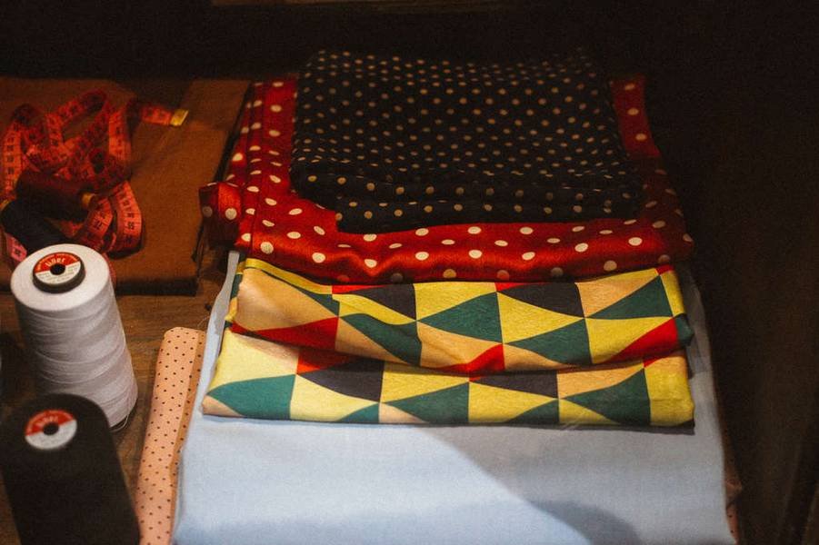 C&aacute;c mẫu vải nhiều m&agrave;u sắc v&agrave; hoa văn được xếp chồng l&ecirc;n nhau, b&ecirc;n cạnh l&agrave; chỉ cuộn v&agrave; thước d&acirc;y.