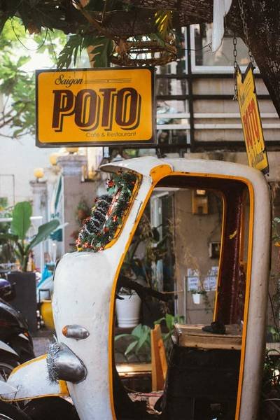 Qu&aacute;n c&agrave; ph&ecirc; với biển hiệu m&agrave;u v&agrave;ng v&agrave; c&aacute;nh cửa xe tuk-tuk cũ trang tr&iacute; c&acirc;y xanh b&ecirc;n trong.