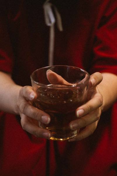 Hai tay đang cầm ly nước m&agrave;u n&acirc;u, nền ph&iacute;a sau l&agrave; &aacute;o đỏ.