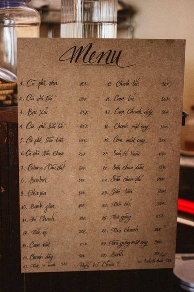 Thực đơn viết tay tr&ecirc;n giấy n&acirc;u với danh s&aacute;ch c&aacute;c loại đồ uống v&agrave; gi&aacute; cả, treo tr&ecirc;n bề mặt gỗ.