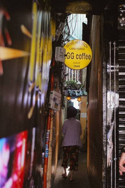 Hẻm nhỏ hẹp với người đi bộ, c&oacute; bảng hiệu qu&aacute;n c&agrave; ph&ecirc; v&agrave; đ&egrave;n trang tr&iacute; treo tr&ecirc;n cao.