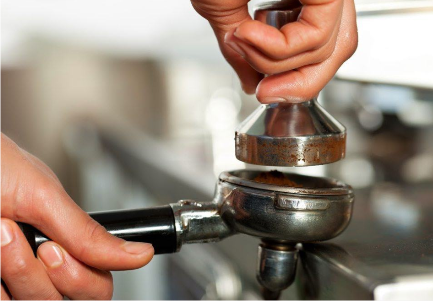 Tay người đang nhấn nén cà phê trong tay cầm máy pha, chuẩn bị làm espresso.