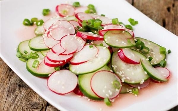 Đĩa salad với lát củ cải đỏ và dưa leo, rắc mè và hành lá, trên nền gỗ.