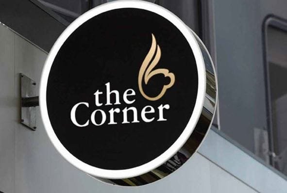 Biển hiệu tròn màu đen với dòng chữ "the Corner" và hình ảnh trang trí màu vàng.