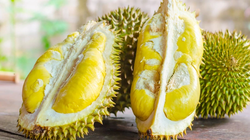 Quả sầu riêng đã bổ đôi, lộ rõ phần thịt vàng bên trong, đặt trên bề mặt gỗ.