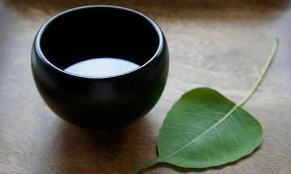 Chiếc b&aacute;t m&agrave;u đen đặt tr&ecirc;n mặt b&agrave;n gỗ cạnh một chiếc l&aacute; xanh.