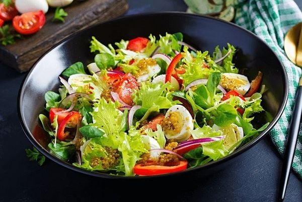 Đĩa salad trộn với rau xanh, cà chua, hành tây, trứng và nước sốt, bày trên bàn với khăn trải màu xanh.