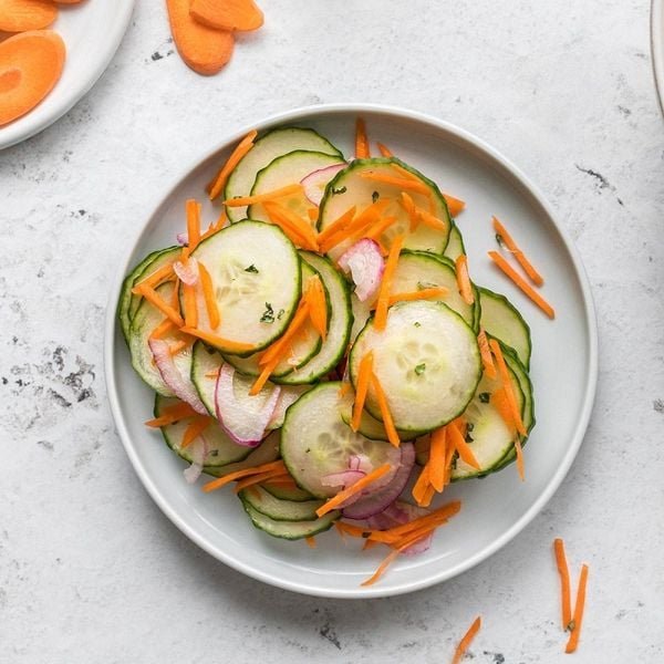 Đĩa salad gồm dưa leo, cà rốt và hành tím thái lát mỏng trên nền bàn màu trắng.