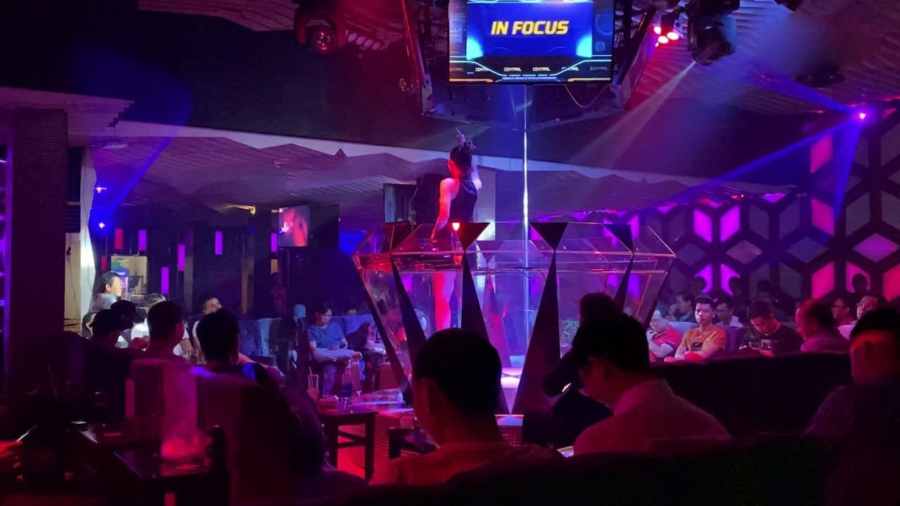 Khung cảnh bên trong một câu lạc bộ đêm với sân khấu và màn hình hiển thị lớn, ánh sáng màu sắc.