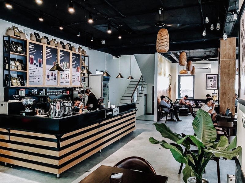 Nhượng quyền cafe Milano có chi phí bao nhiêu? Có nên không? 8 Quán cà phê với quầy pha chế hiện đại, khách hàng ngồi thư giãn, trang trí đèn treo và cây xanh.