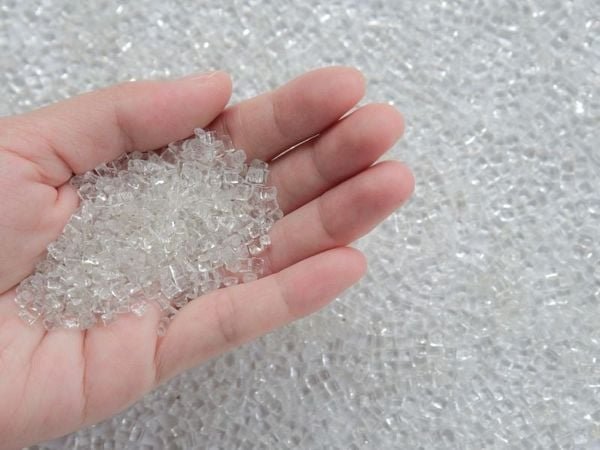 B&agrave;n tay đang cầm nhiều hạt nhựa trong suốt, nằm tr&ecirc;n nền cũng c&oacute; nhiều hạt nhựa tương tự.