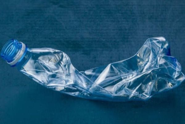 Chai nhựa trong suốt bị b&oacute;p m&eacute;o, nằm tr&ecirc;n nền m&agrave;u xanh tối.