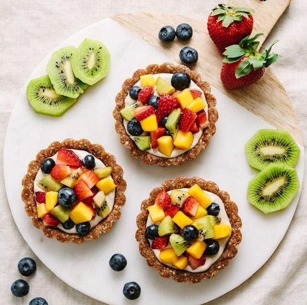 Ba chiếc b&aacute;nh tart tr&aacute;i c&acirc;y với kiwi, d&acirc;u t&acirc;y, việt quất v&agrave; xo&agrave;i tr&ecirc;n đĩa tr&ograve;n trắng. C&oacute; l&aacute;t kiwi v&agrave; d&acirc;u t&acirc;y b&ecirc;n cạnh.