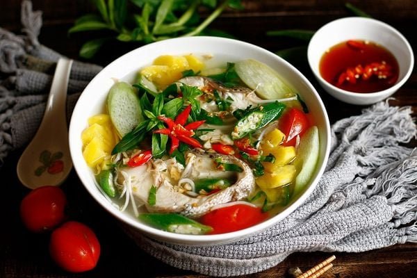 B&aacute;t b&uacute;n c&aacute; với rau thơm, c&agrave; chua, dứa, ớt v&agrave; đĩa nước mắm ớt b&ecirc;n cạnh tr&ecirc;n nền khăn x&aacute;m.