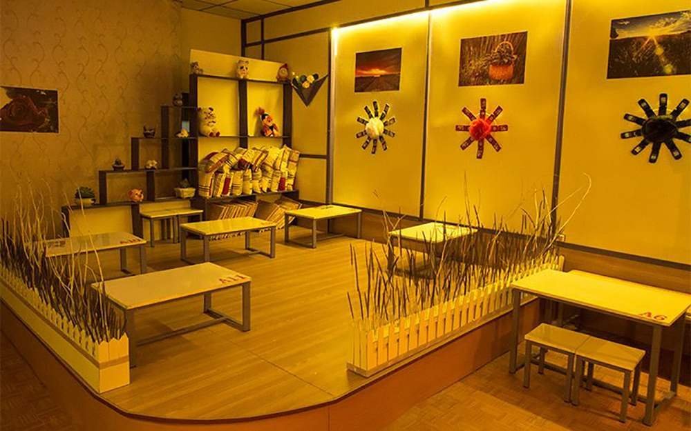 Quán cà phê với bảng hiệu đèn neon sáng, xe đạp treo phía trên, cây xanh và xe máy đậu trước cửa vào ban đêm.