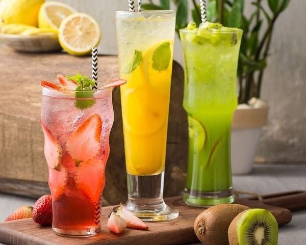 tra-hoa-qua-1_eee3c25aa62c4dbeb7_aa62344dcffc4ee5bc9fdea0aa4b4895_grande Ba ly nước trái cây màu sắc khác nhau, trang trí với lát trái cây và ống hút, đặt trên bàn gỗ.