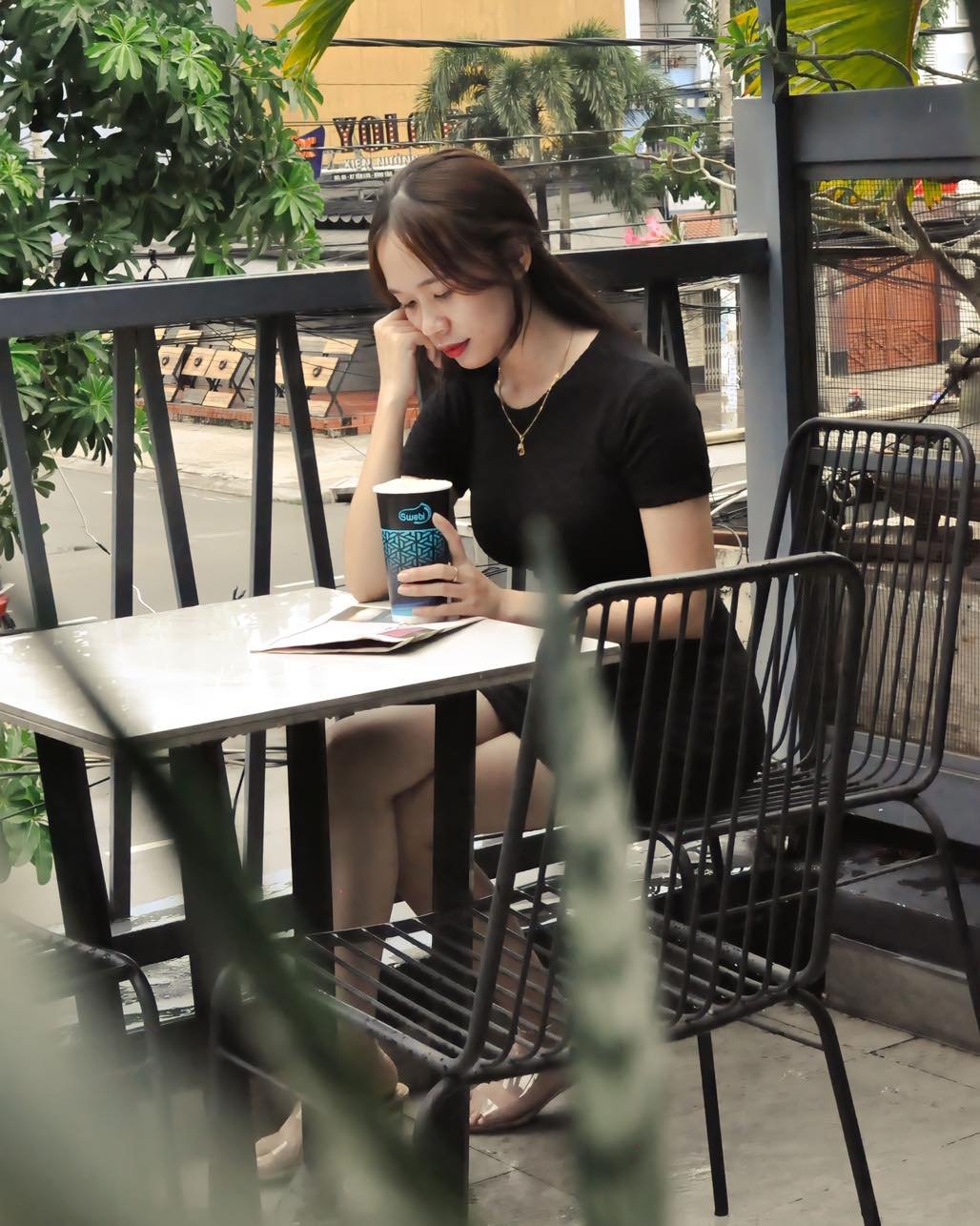 Một người ngồi trong quán cà phê, cầm ly nước, nhìn ra ngoài qua cửa sổ với vẻ mặt suy tư.