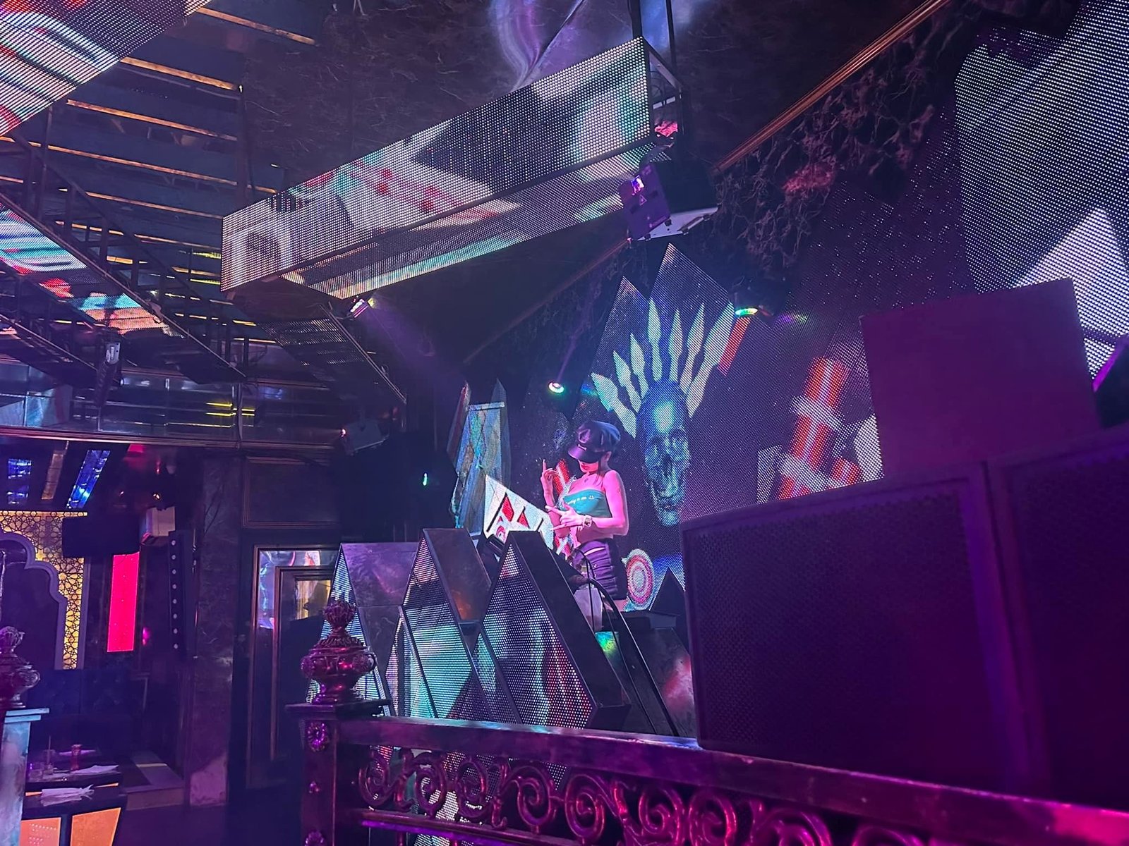 DJ biểu diễn trên sân khấu với hình ảnh đồ họa sống động và ánh sáng màu sắc trong không gian hộp đêm.