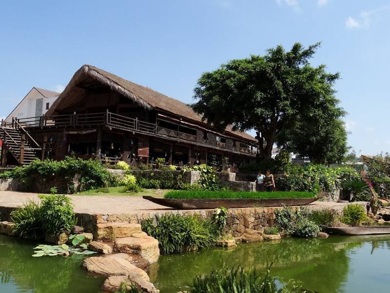 Ng&ocirc;i nh&agrave; gỗ lớn với m&aacute;i tranh, xung quanh l&agrave; c&acirc;y xanh v&agrave; hồ nước, tạo n&ecirc;n khung cảnh thi&ecirc;n nhi&ecirc;n y&ecirc;n b&igrave;nh.