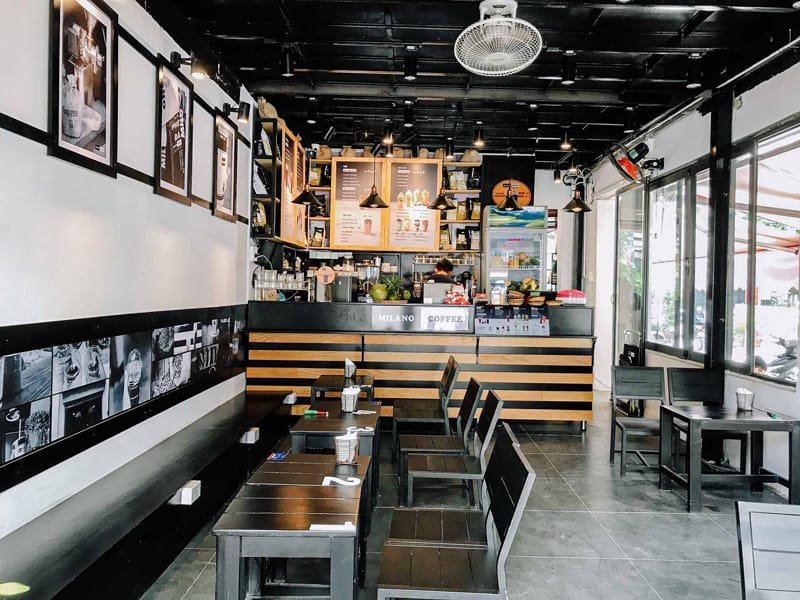 Nhượng quyền cafe Milano có chi phí bao nhiêu? Có nên không? 3 Quán cà phê với bàn ghế gỗ, tường trang trí ảnh, quầy pha chế có thực đơn treo phía trên, không gian sáng sủa.