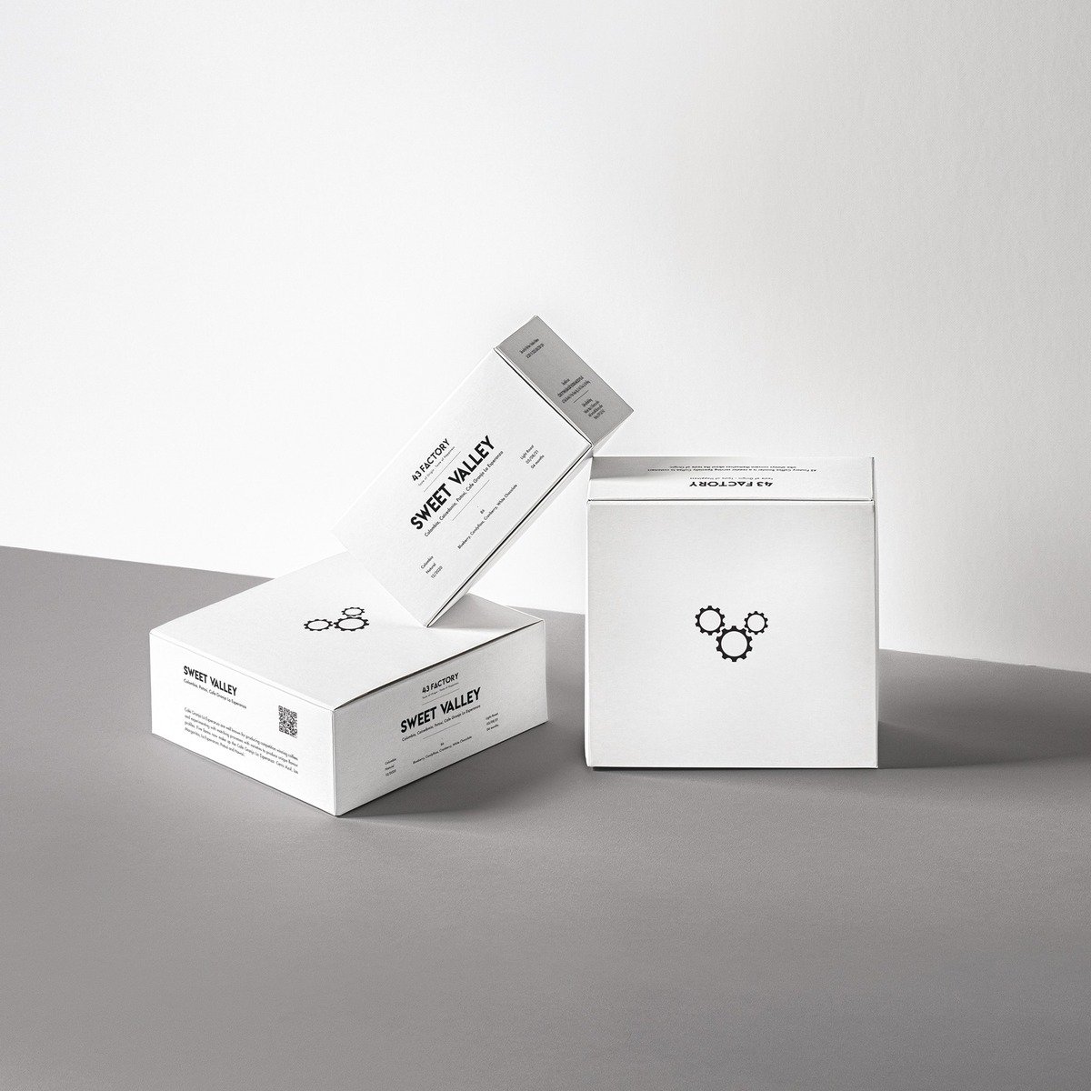 C&aacute;c hộp giấy m&agrave;u trắng được xếp chồng l&ecirc;n nhau tr&ecirc;n bề mặt m&agrave;u x&aacute;m, c&oacute; thiết kế đơn giản v&agrave; biểu tượng in tr&ecirc;n mặt trước.