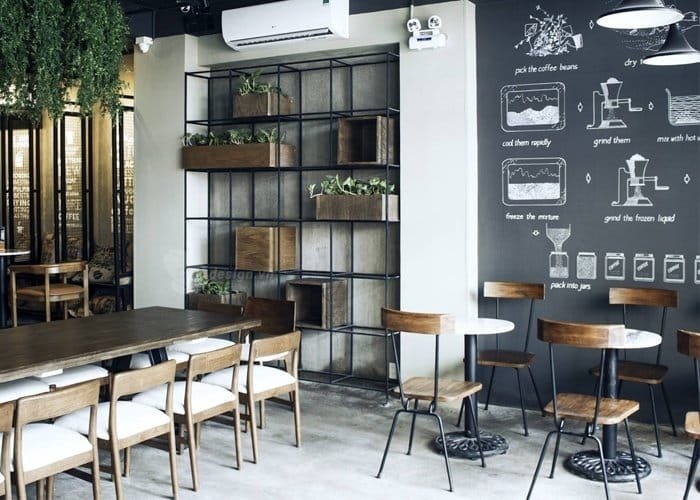 Nhượng quyền cafe Milano có chi phí bao nhiêu? Có nên không? 9 Quán cà phê hiện đại với bàn ghế gỗ, kệ trang trí cây xanh và bảng đen có hình vẽ minh họa quy trình pha cà phê.