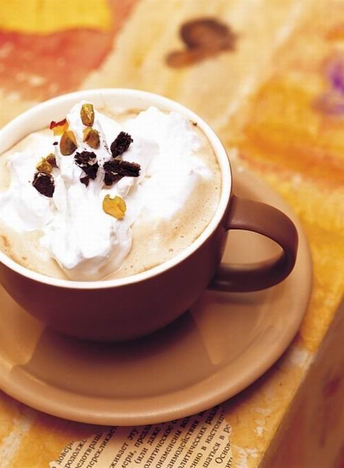 Tách cà phê với kem tươi và hạt trang trí trên bàn gỗ có tông màu ấm áp.