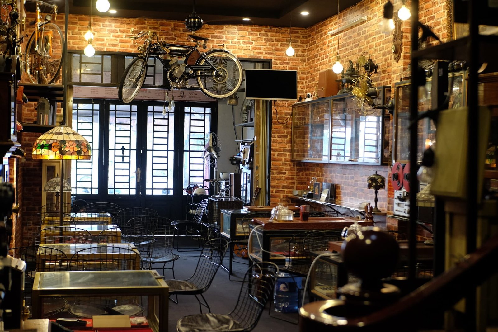 Quán cà phê phong cách cổ điển với tường gạch, xe đạp treo và nội thất trang trí đèn cổ.