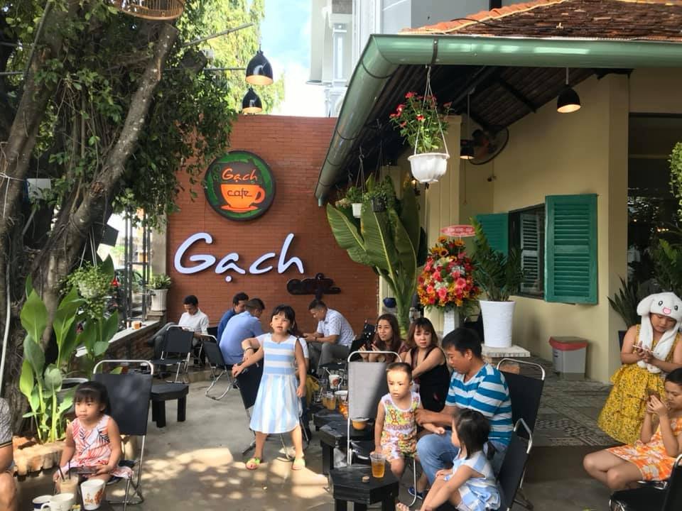 Top 32 thương hiệu nhượng quyền cafe siêu lợi nhuận 20 Quán cà phê ngoài trời với nhiều người ngồi uống nước, cây xanh và hoa trang trí xung quanh.
