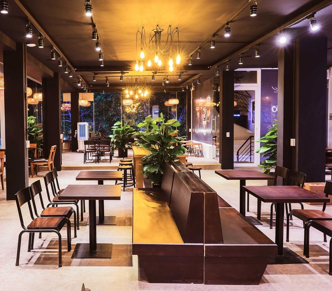 Nhượng quyền cafe Milano có chi phí bao nhiêu? Có nên không? 6 Quán cà phê hiện đại với bàn ghế gỗ, ánh sáng ấm áp và cây xanh trang trí tạo không gian thoải mái.