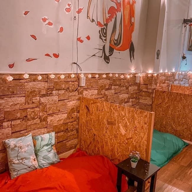 Góc phòng nhỏ với giường nệm, tường trang trí tranh và đèn dây, tạo không gian ấm cúng và thư giãn.