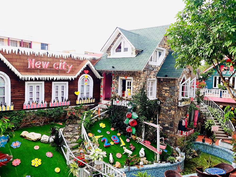 Ng&ocirc;i nh&agrave; đ&aacute; với m&aacute;i xanh, trang tr&iacute; s&acirc;n vườn bằng hoa v&agrave; tượng động vật, c&oacute; biển chữ "New city".