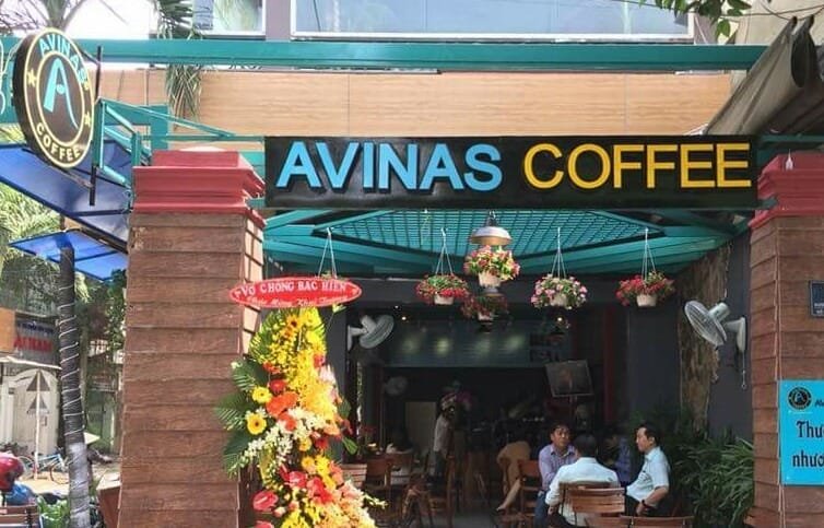 Top 32 thương hiệu nhượng quyền cafe siêu lợi nhuận 32 Quán cà phê với bảng hiệu "AVINAS COFFEE", có trang trí hoa và khách hàng ngồi bên trong.